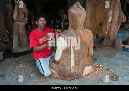Eine balinesische Handwerker Holzschnitzer bei der Arbeit auf ein schnitzen eines großen sitzenden Buddha in dem Dorf Peliatan Stockfoto