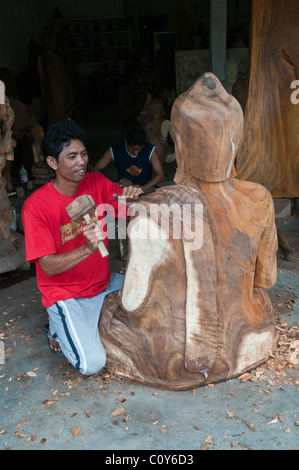 Eine balinesische Handwerker Holzschnitzer bei der Arbeit auf ein schnitzen eines großen sitzenden Buddha in dem Dorf Peliatan Stockfoto