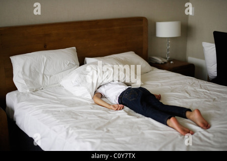 Mädchen liegt auf Bauch im Bett mit Kopf unter Kopfkissen Stockfoto