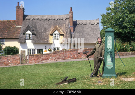 Schornsteinfeger posiert neben historischen Wasserpumpe auf Monks Eleigh Village Green Property name Beyond Digital Suffolk East Anglia England UK entfernt Stockfoto