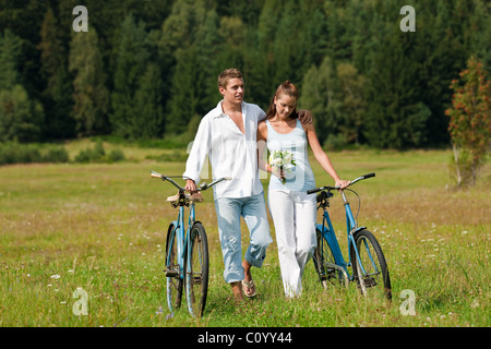 Romantische junge Paare, die mit alten Motorrad auf Wiese an sonnigen Tag Stockfoto