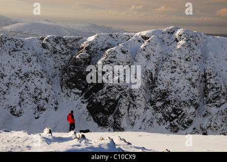 Walker in rote Jacke mit Blick auf Dow Crag von Coniston Greis im Winter im englischen Lake District Stockfoto