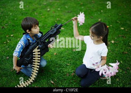 Fünf Jahre altes Mädchen legt Blumen im Lauf ihres Bruders Spielzeug Maschine Pistole Stockfoto