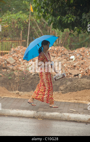 Myanmar (aka Burma), Yangon (aka Rangoon). Frau in traditioneller Kleidung mit Regenschirm. Stockfoto