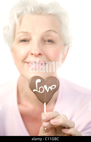 Eine reife Frau mit einem Schokoladen Herz mit dem Wort "Liebe" in der hand Stockfoto