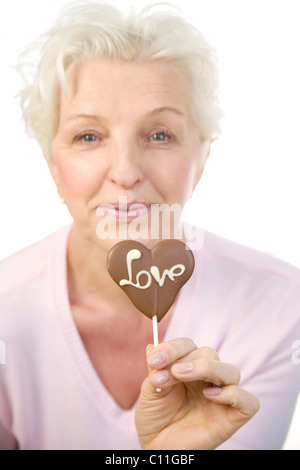 Eine reife Frau mit einem Schokoladen Herz mit dem Wort "Liebe" in der hand Stockfoto