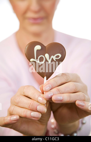 Eine reife Frau mit einem Schokoladen Herz mit dem Wort "Liebe" in der hand Stockfoto