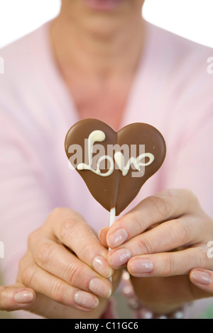 Eine reife Frau mit einem Schokoladen Herz mit dem Wort "Liebe" in der hand Stockfoto