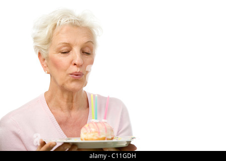 Eine reife Frau Ausblasen der Kerzen auf einem donut Stockfoto