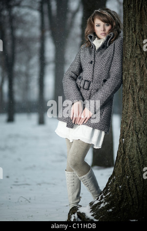 Junge Frau, die an einen Baumstamm gelehnt Stockfoto