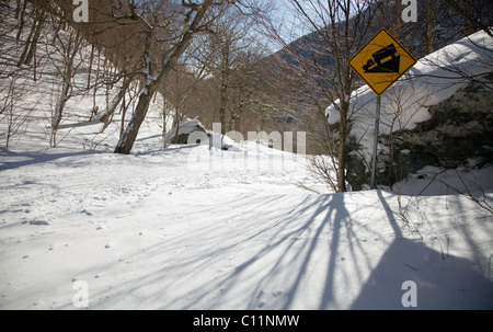 Schmale Bergstraße im Schnee mit einem Warnhinweis bedeckt. Stockfoto