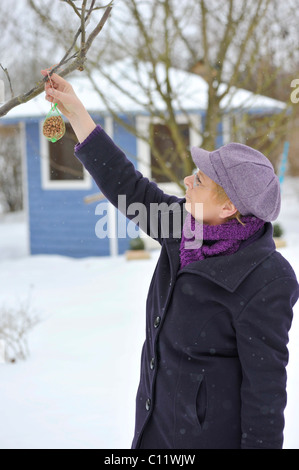 Frau eine Tasche von Erdnüssen auf einem Baum als eine Winterfütterung für Vögel hängen Stockfoto