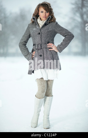 Junge Frau im Schnee, trägt eine Jacke, Strumpfhosen und Stiefeln Stockfoto