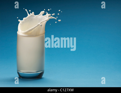 Spritzer Milch aus dem Glas auf blauem Hintergrund Stockfoto