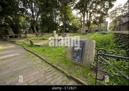 Eingang zum Friedhof mit Kopfsteinpflaster, Infotafel, Grabsteine und Gräber, Pfarrhaus Beyond - St. Michael & All Angels Church, Haworth, West Yorkshire, England, Großbritannien. Stockfoto