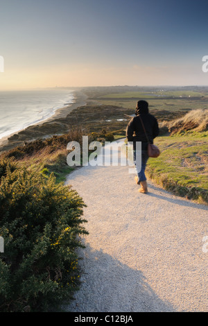 Eine Frau geht den Weg am Hengistbury Head, auf einen Winter Sonnenuntergang genommen. Stockfoto