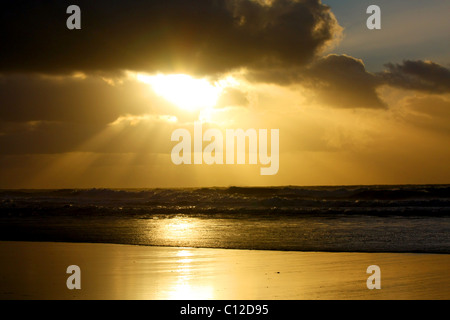 Ein 40,151.06066 Sonnenstrahlen Sonnenstrahlen dunkle Wolken Wolkenschichten goldenen Glanz strahlenden Sonnenlicht auf Wellen Strand. Stockfoto