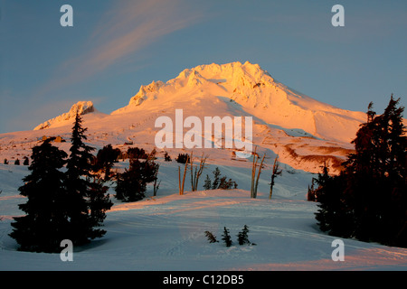 40,171.06371 a A snowy gezackte spitze Gipfel mit einer hellen, gelblich leuchten in einem weißen Winter Sonnenuntergang gegen ein weiches baby blue sky. Stockfoto