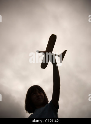 Ein Zehn Jahres altes Mädchen hält ein Spielflugzeug Balsa Holz, wie sie vor einem dunklen und trüben Himmel abhebt ist. Stockfoto