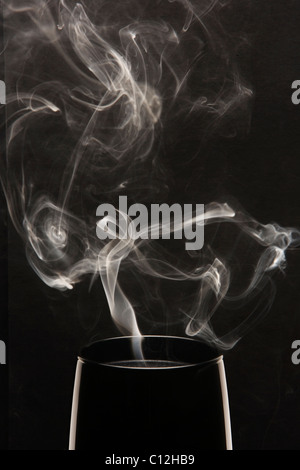 Weißer Rauch steigt aus einer schwarzen Kerze vor einem schwarzen Hintergrund. Stockfoto