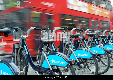 Eine verschwommene rote London Bus vorbei ein Rack mit Boris Bikes Stockfoto