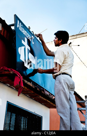 Vorsatz junge mexikanische Zeichen malen Maler Künstler auf Leiter funktioniert per Hand auf Schriftzug Zeichen Grafiken für christliche Gruppe in Oaxaca Stockfoto