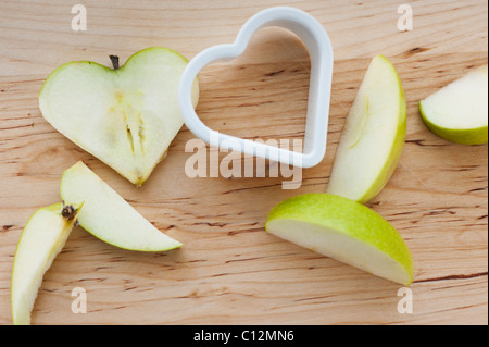 Herzförmige Äpfel mit Cutter auf Schneidebrett Stockfoto