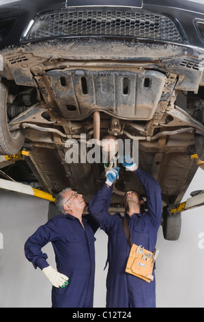 Kfz-Mechaniker mit Lehrling arbeitet unter einem erhöhten Auto in einer garage Stockfoto