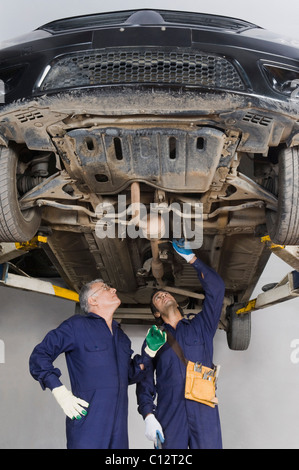 Kfz-Mechaniker mit Lehrling arbeitet unter einem erhöhten Auto in einer garage Stockfoto