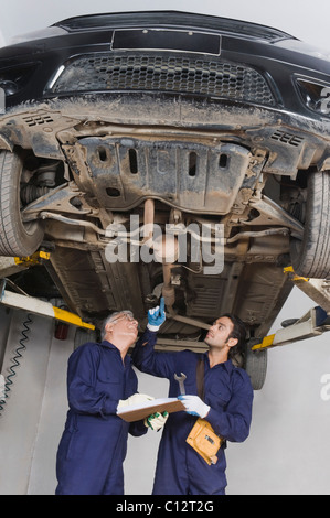 Kfz-Mechaniker mit Lehrling arbeitet unter einem erhöhten Auto in einer garage Stockfoto