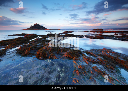 St. Michaels Mount im Schein der Morgensonne beleuchtet. Die zurückweichenden Flut schafft Fels-Pools, die den Sonnenaufgang Himmel widerspiegeln. Stockfoto