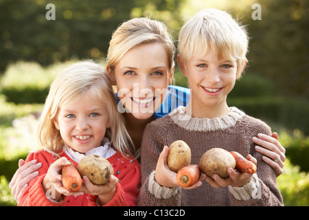 Junge Mutter und Kinder im Garten Pose mit Gemüse Stockfoto