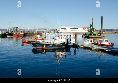 Sammlung von kleinen Arbeitsboote vertäut im Hafen von Stranraer mit Larne Fähre im Hintergrund Stockfoto