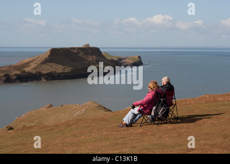 Älteres Ehepaar sitzen, mit Blick auf Worms Head, Rhossili, Gower, UK, genießen die Aussicht in Ruhe Stockfoto