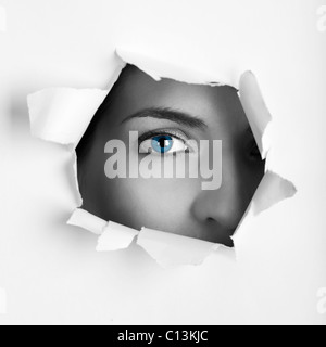 Schöne weibliche blaue Augen Blick durch ein Loch auf einem Blatt Papier Stockfoto