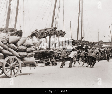 Bande von fünf chinesischen Dock Arbeiter Lean hart an Seilen, eine schwere Wagenladung von Säcken am Hong Kong Wasser zu schleppen. Zwischen 1890 und 1923. Stockfoto