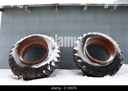 Großer Traktorreifen mit Felge stützte sich auf Zinn vergossen im Schnee Stockfoto