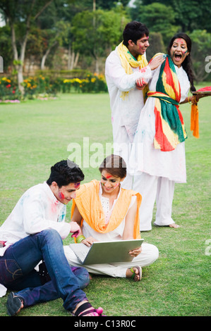Paar mit einem Laptop mit ihren Freunden feiern Holi dahinter Stockfoto