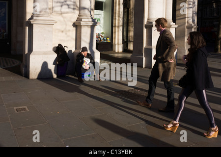 Ein schlafender Big Issue Magazin Verkäufer sitzt alleine ohne Weitergabe auf Zuschauer verächtlich in London vorbei. Stockfoto