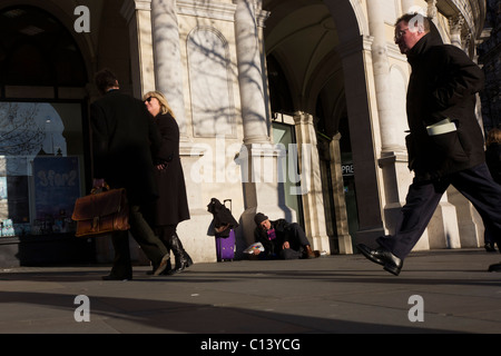 Ein schlafender Big Issue Magazin Verkäufer sitzt alleine ohne Geschäft als desinteressiert auf Zuschauer Pass-by in London übergeben. Stockfoto