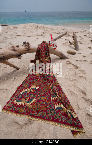 Eine Batik-Sarong drapiert über Treibholz auf dem weißen Sand Strand von Bias Tegal in Padang Bai auf Bali Stockfoto