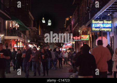 Menschen trinken und Wandern entlang der Bourbon Street in New Orleans mit Leuchtreklamen Stockfoto