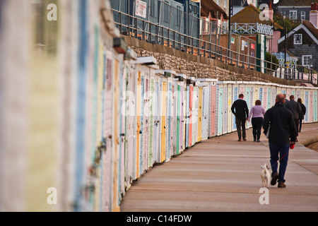 Am frühen Morgen Wanderer entlang der Promenade in Lyme Regis in Dorset. Neben ihnen sind Reihen von bunten Strandhäuschen. Stockfoto