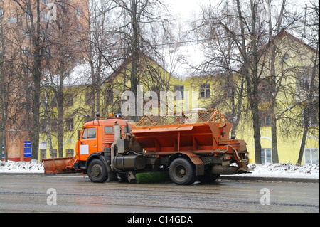 Der LKW reinigt Straße aus einer Schmutz und Schnee gegen das gelbe Haus in einer Stadt Domodedovo, Moskau, Russland Stockfoto