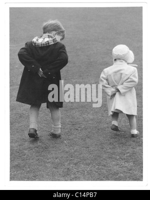 Original-charmantes Foto von zwei süßen kleinen Kindern, möglicherweise älterer Bruder mit jüngerer Schwester, die beide mit den Händen hinter dem Rücken laufen - um die 1950er Jahre, Großbritannien Stockfoto