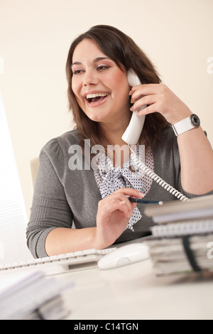 Lächelnde Sekretärin am Telefon im modernen Büro am Schreibtisch Stockfoto