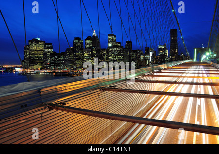 Autos fahren in der Abenddämmerung, New York über die Brooklyn Bridge mit der New Yorker Skyline im Hintergrund. Stockfoto