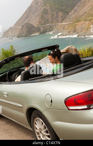 Paar sitzt in einem silbernen Cabrio mit Blick auf die Küste in Big Sur, Kalifornien während des Lesens einer Karte Stockfoto