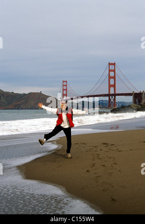 Golden Gate Bridge, San Francisco, Kalifornien. Chinesische Frau springt vor Freude unter der Golden Gate Bridge am Baker Beach Stockfoto