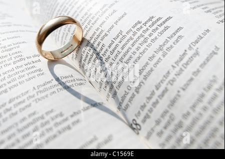 Ein Ehering wirft einen Schatten auf den offenen Seiten eines aufgeschlagenen Buches religiöse Stockfoto